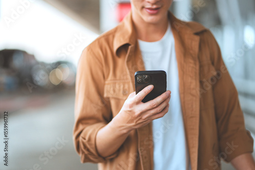 Close-up portrait of happy asian man smiling while booking flight tickets on airline website using smartphone – planning travel abroad with mobile technology and fast 5G internet connection