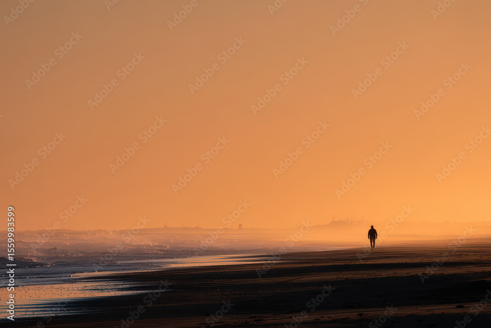 Fototapeta premium serene scene of solitary figure walking along deserted beach at golden hour
