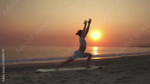 Woman Practicing Warrior I Yoga Pose at Sunrise on the Beach