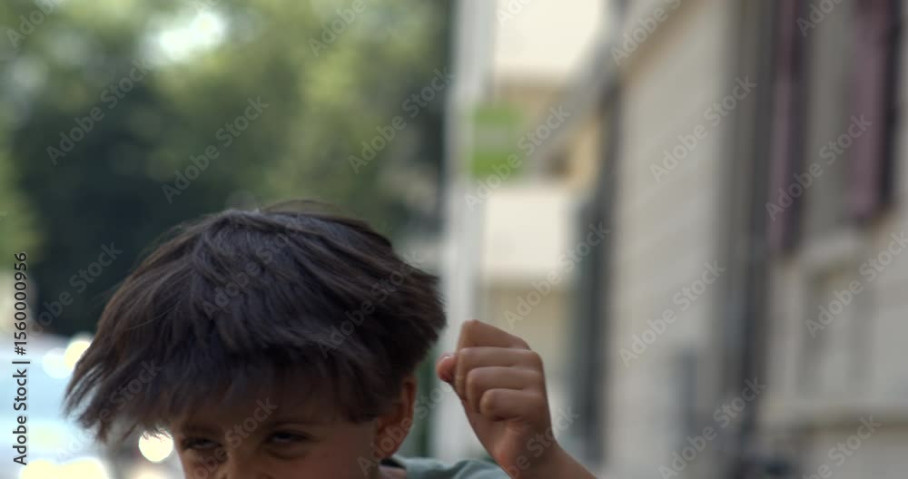 Young boy laughing wildly mid-air with hair lifted and mouth open, caught in burst of playful energy in super slow motion on city street