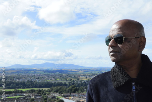Confident Man Overlooking Enniscorthy Town from Vinegar Hill Summit, County Wexford, Ireland on a Bright Sunny Evening – Panoramic Hilltop View with Lush Green Fields and Rolling Hills