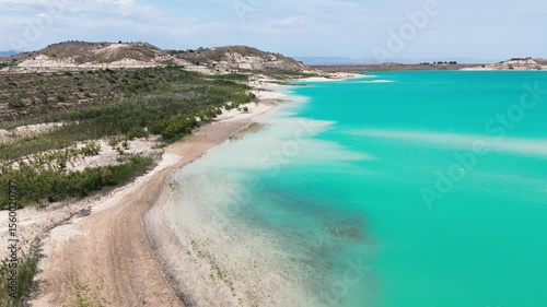 Aerial view of Embalse de La Pedrera reservoir landscape, with striking turquoise waters, curving white-sand shores, and desert-like hills. Costa Blanca. Province of Alicante. Spain	