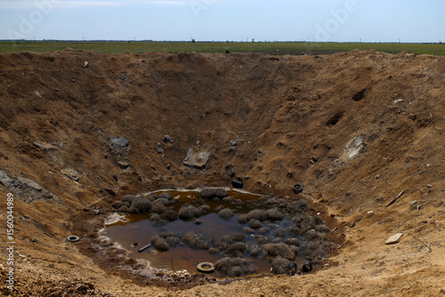 A huge, devastating crater formed after the explosion of a fertilizer depot in Ukraine, caused by a powerful Russian missile strike, leaving a massive impact zone and significant destruction in the su