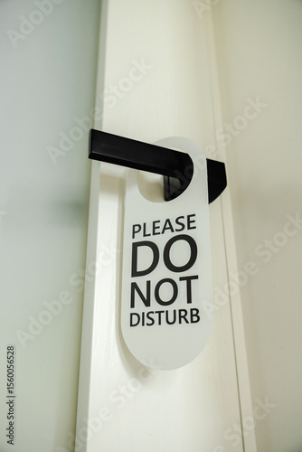 Modern black door handle with a white hanging sign that reads Please Do Not Disturb in bold black letters photo