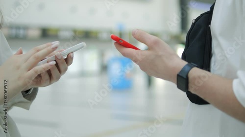 Two people are talking on their cell phones in a public place. One of the phones is red