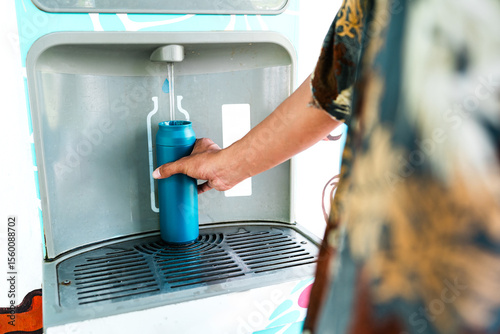 Refillable water bottle being filled at eco-friendly hydration station. Close-up of hand refilling water bottle outdoors at green campus station.