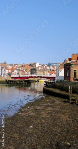 Portrait vertical footage of the seaside town of Whitby in the UK showing the river going out to sea and the main bridge with traffic going over the bridge on a sunny day in the summer time