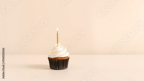 Elegant single cupcake with white icing and gold candle in corner on soft cream background for text

