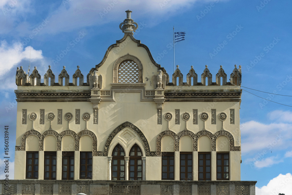 Naklejka premium Close-up of a historic building in Rhodes, Greece, façade displays decorative arched windows, intricate stucco reliefs, circular motifs, and crenellated roof details