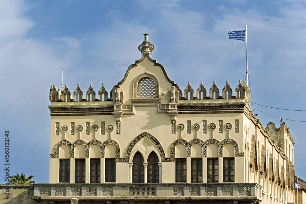 Fototapeta premium Close-up of a historic building in Rhodes, Greece, façade displays decorative arched windows, intricate stucco reliefs, circular motifs, and crenellated roof details