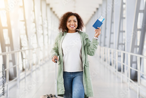 Ready For Trip. Smiling young Black woman at airport holding passport and ticket, joyful and confident travel moment in modern terminal with bright lighting, copy space