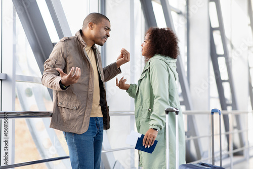 Young Black couple arguing in airport, having intense conversation, upset expressions, holding travel documents, emotional travel moment with tension or disagreement