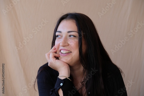 A woman with long dark hair is sitting laughing and white teeth are visible
