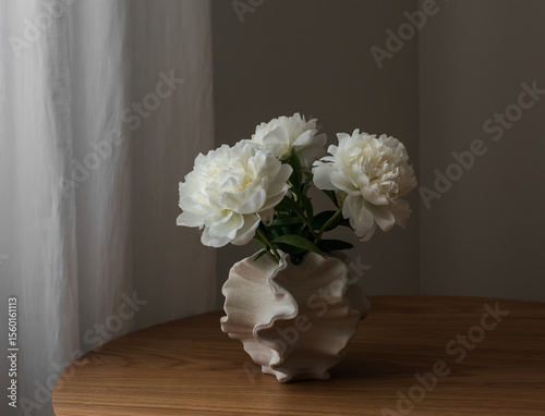 Fototapeta Naklejka Na Ścianę i Meble -  A bouquet of white peonies in a ceramic vase on a wooden table in the living room