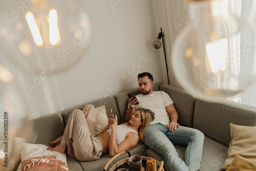 Foto Couple Relaxing on Sofa at Home Using Smartphones with Snacks Nearby
