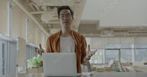 Senior Asian businessman wearing headset celebrates success during online meeting in modern co-working space. Remote work and business communication concept.