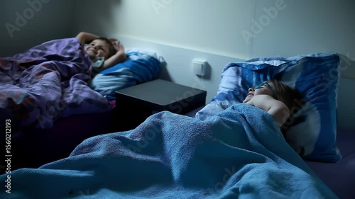 A caring little boy turns off the lamp, ready for sleep with his sister in a cozy camper van bedroom during their family holiday. Sweet childhood moment