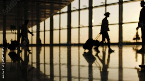 Silhouetted travelers pulling wheeled luggage crossing sunlit airport terminal, capturing travel anticipation and movement during golden hour