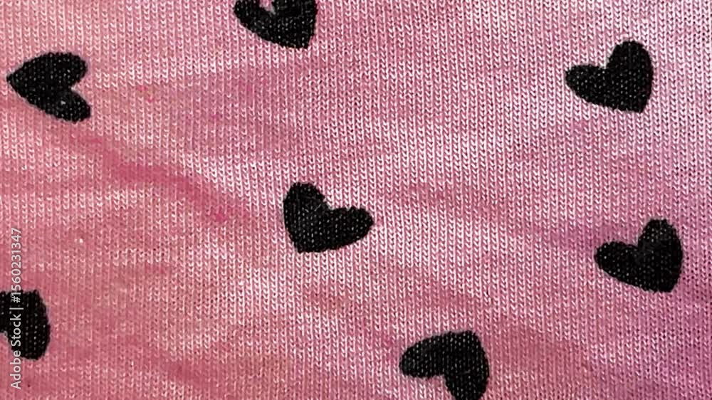 Close-up of pink knitted fabric with black heart pattern. A cute and romantic textile background loop with a sweet, playful aesthetic