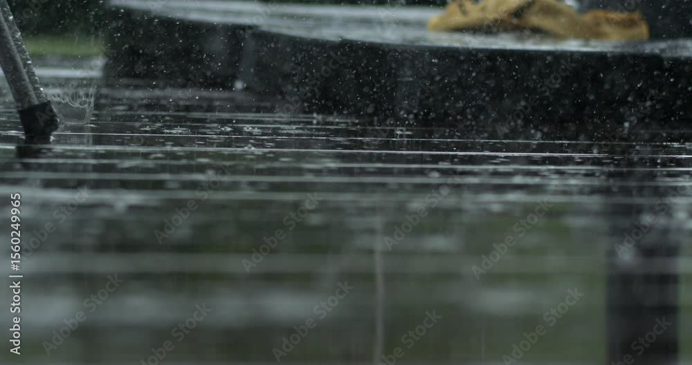 Slow motion rain captured with high speed camera bouncing off deck, with distant table and chair in background, soft focus and detailed water patterns