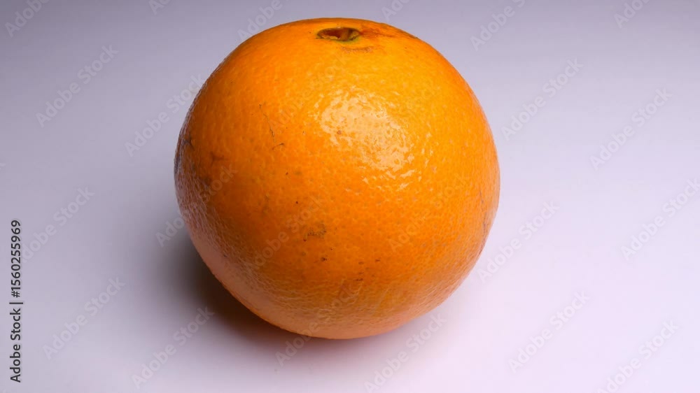 An orange in a white background. The light source slowly moves above the fruit slightly changing the shadows.