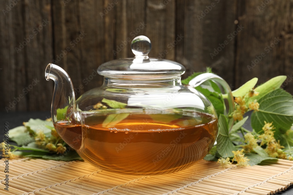 Tasty linden tea in teapot, leaves and flowers on table against wooden background, closeup Tasty linden tea in teapot, leaves and flowers on table against wooden background, closeup
