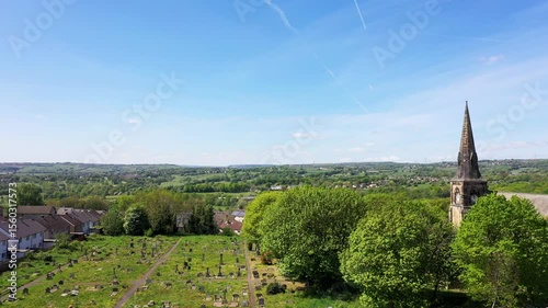Aerial footage of the city of Bradford in the UK showing a church with cemetery and fields on a bright sunny summers day along side a housing estate