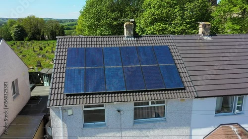 Aerial drone footage of a British semi detached house with energy saving solar panels on the roof on a sunny summers day located with a grave yard behind the house