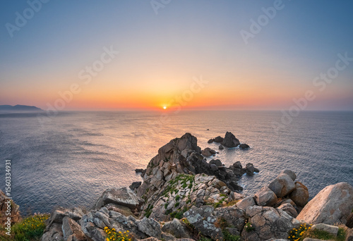 Sunset over Estaca de Bares Galicia rocky headland facing Atlantic calm waves glowing sky massive boulders in foreground peaceful scene freedom solitude strength