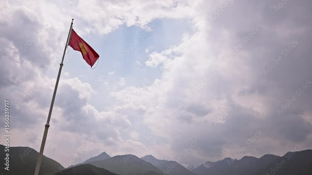 national flag of Kyrgyzstan swaying in the wind before the storm with mountain range on the horizon