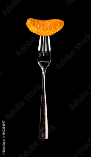 Suspended chrome fork with luminescent orange slice attached to tines on black background