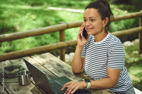 Person Working Outdoors with a Laptop While Talking on the Phone, Surrounded by Nature