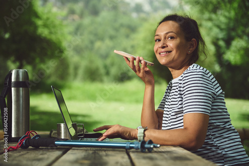 Woman Smiling While Voice Recording in Nature with Laptop and Hiking Gear