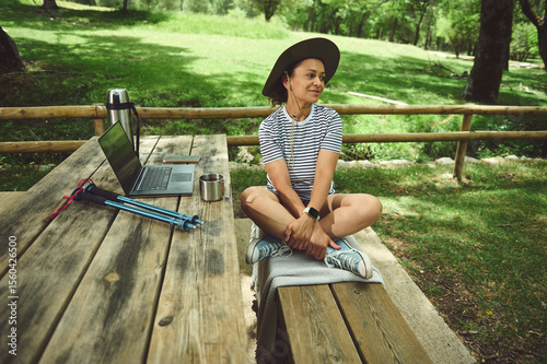Woman Relaxing Outdoors at Picnic Table with Laptop in a Scenic Forest