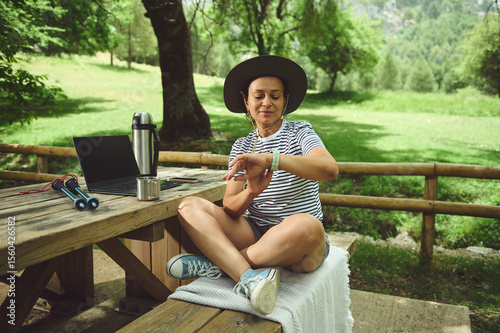 Woman Relaxing Outdoors Using Smartwatch and Laptop in Tranquil Nature