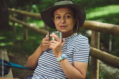 Woman Relaxing Outdoors with a Mug Amidst Nature, Wearing a Hat and Enjoying Summer
