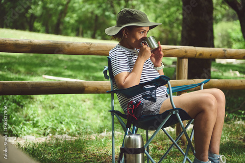 Woman Relaxing Outdoors Drinking From A Mug In A Scenic Forest Setting