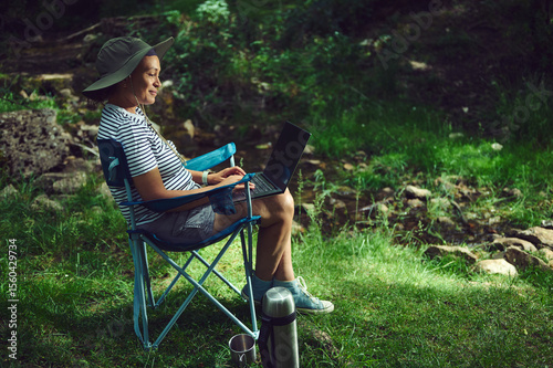 Person Working Outdoors on Laptop with Nature Background, Embracing Work and Relaxation