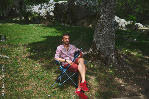 Man Relaxing on a Camping Chair Under a Tree in a Beautiful Park