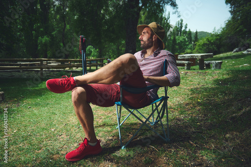 Man Relaxing Outdoors in Camping Chair on a Sunny Day Amidst Lush Trees and Tranquil Nature Setting