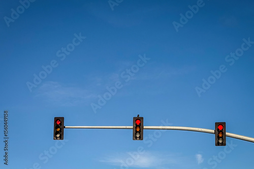 Three traffic lights hang on a horizontal pole against a vibrant blue sky on a clear day in the United States. Minimalist composition with strong contrast and copy space.