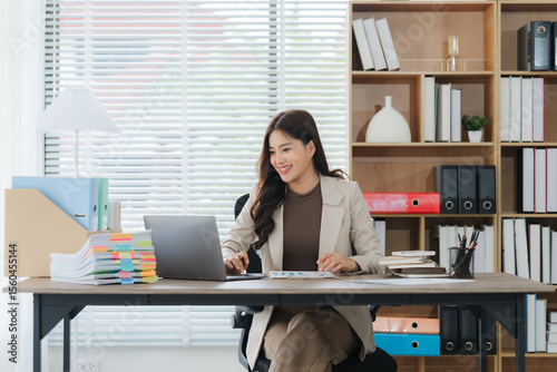 Smiling Businesswoman Working on Laptop: A cheerful businesswoman smiles while working on her laptop at her organized desk in a modern office.  She exudes confidence and productivity.