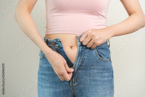 Fat belly, chubby asian young woman trying to zip it up tight jeans, obese girl excess fat around waist due to weight gain and a belly. Diet lifestyle and health care concept isolated on background