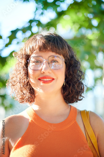 Real beauty of a confident and empowered smiley young woman with wavy hair, glasses, and bright red lipstick. Body acceptance concept.