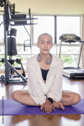 Non-binary gay man with mustache and androgynous appearance working out indoors in gym. Wearing feminine sports bra and using water bottle. Inclusive fitness concept with genderfluid representation.