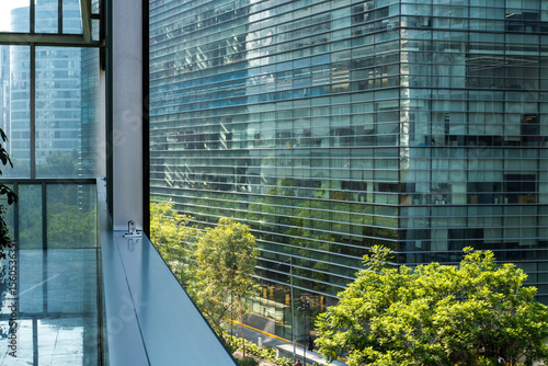 Modern urban architecture framed by reflections and lush green trees, blending natural and artificial urban surfaces into an abstract pattern of color, rhythm and geometry under vivid daylight.