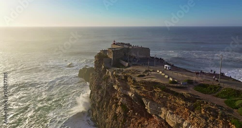 Aerial view of the lighthouse located on a huge cliff and offering a view of the huge ocean waves of Nazare, Portugal