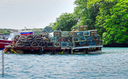 Lobster traps stacked on a boat in a calm harbor surrounded by greenery during daytime