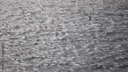 Silhouette of a kite surfer riding the waves of the ocean in the golden hour of dawn. The parachute is clearly visible in the sky, the athlete glides spectacularly on the water, creating an atmosphere