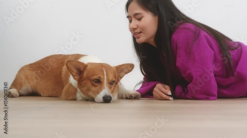 Asian young woman sits on the floor beside her sofa, gently stroking her Corgi dog head relax at home, reflecting warmth, pet lover, the comfort of home life.